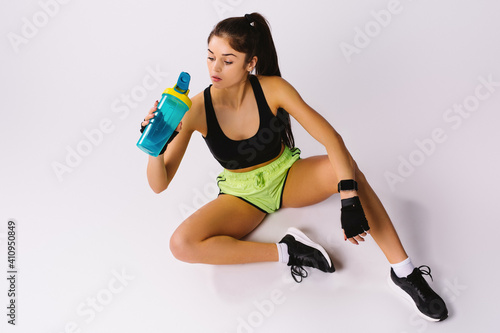 A muscular girl in sportswear drinks a protein shake after a workout. Isolated on a white background.