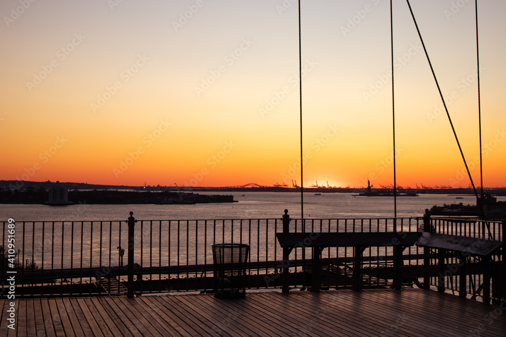 Obraz premium Beautiful Sunset on the East River in New York City with the Silhouette of the Statue of Liberty in the Distance seen from the Brooklyn Bridge