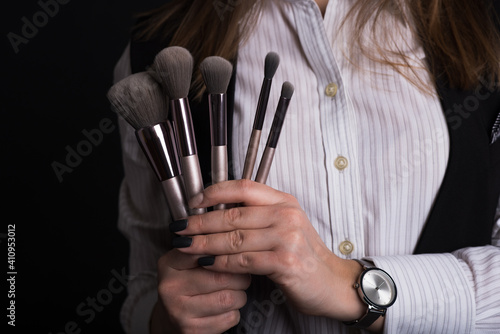 Girl make-up artist holds brushes for visage. Close-up photo in studio on black background