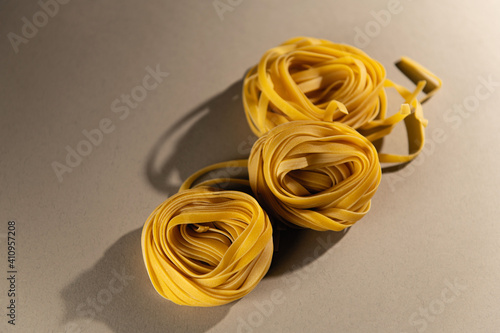 Homemade pasta rolled into nests on a light background. Hard shadow. View from above