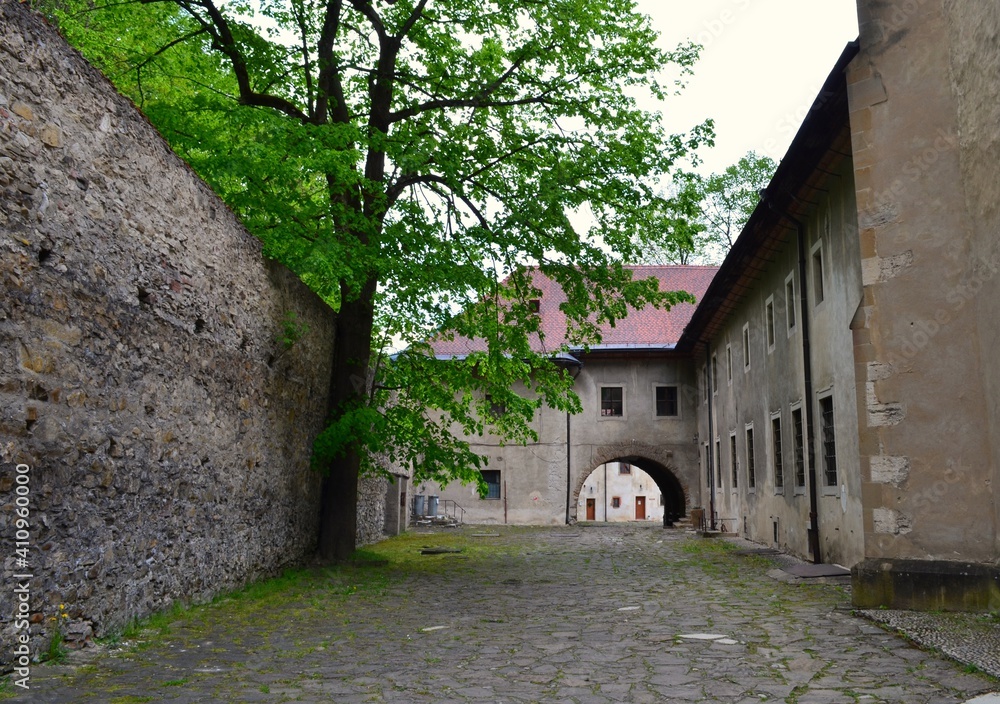 passage between monastic buildings arch stone wall green tree red monastery slovakia spring