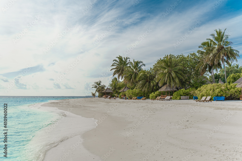 Traumhafter Strand mit Palmen und Sonnenliegen auf einer kleinen Insel auf den Malediven, im Hintergrund blauer Himmel