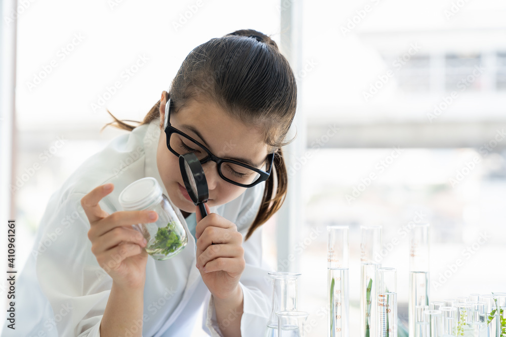 Child girl exploring germs through magnifying glass in glassware at laboratory. Child girl learning science and doing analysis in classroom. Scientific experiment. Early development of children Child girl exploring germs through magnifying glass in glassware at laboratory. Child girl learning science and doing analysis in classroom. Scientific experiment. Early development of children
