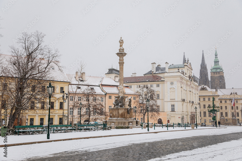 Castle from Hradcany Square, spiers of st Vitus cathedral, archbishop's palace and Marian Plague Column, snow in winter day, Hradcanske namesti, Prague, Czech Republic