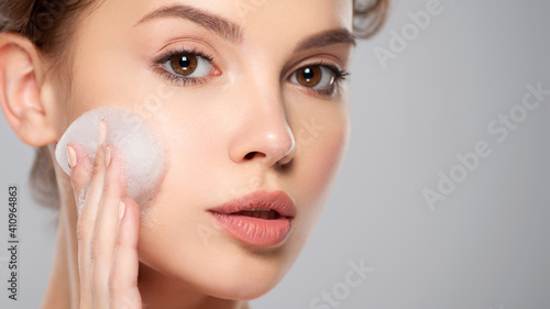 Girl moistens her face.   Woman with soap foam street. Beautiful face of young caucasian woman with perfect healthy skin, isolated.   Pretty white model caring of face. Skin care concept.