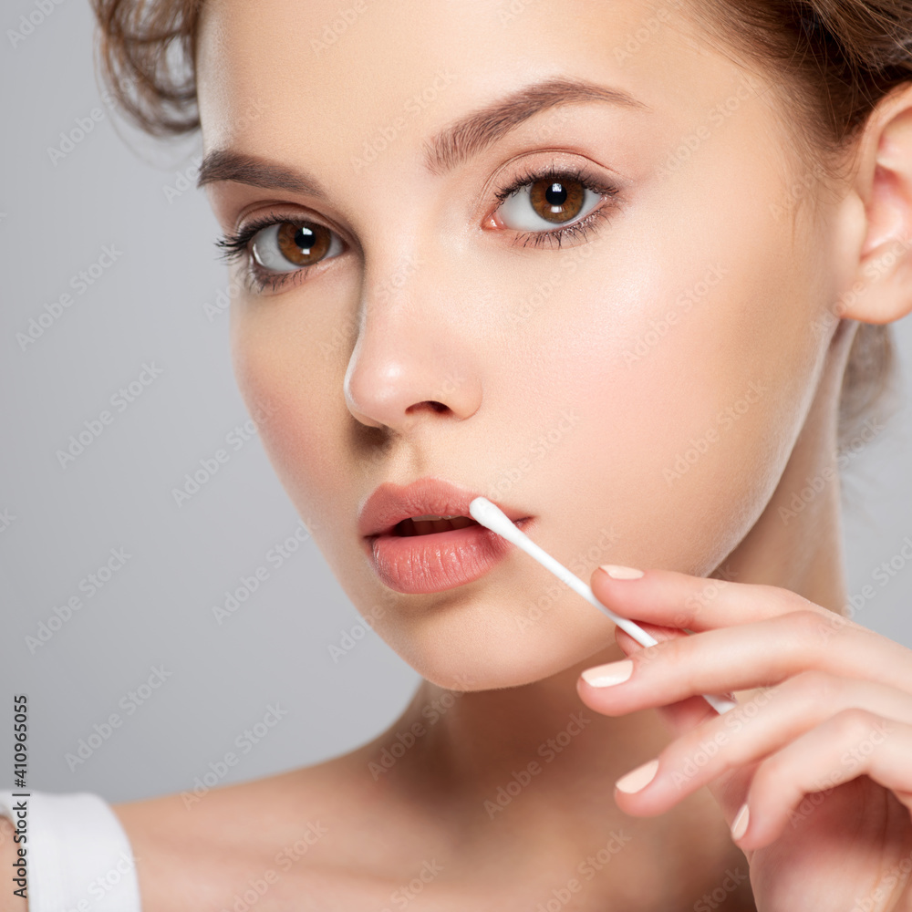 Beautiful face of a young woman with a cotton stick in her hand, isolated. Removing makeup with a cotton stick near lip. Beautiful face of a young woman with a cotton stick in her hand, isolated. Removing makeup with a cotton stick near lip.