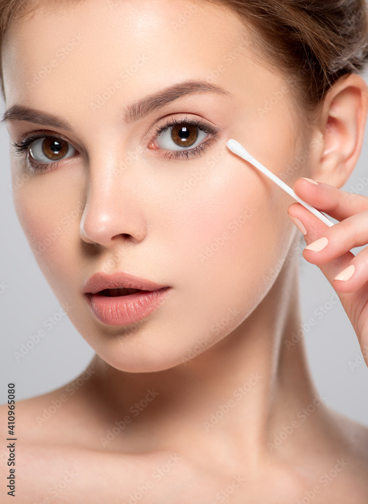 Beautiful face of a young  woman with a cotton stick in her hand, isolated.  Removing makeup with a cotton stick near eyes