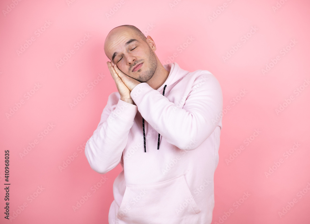 Young bald man wearing casual sweatshirt over pink isolated background sleeping tired dreaming and posing with hands together while smiling with closed eyes. Young bald man wearing casual sweatshirt over pink isolated background sleeping tired dreaming and posing with hands together while smiling with closed eyes.