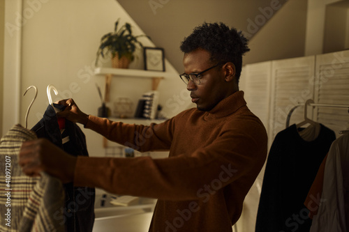 Canvas Print Nervous geeky young black male going out, deciding what to wear, posing indoors