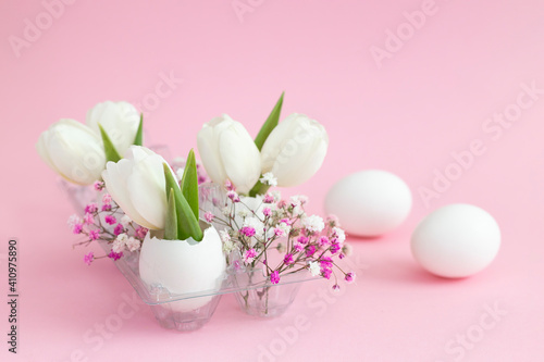 Easter holiday decoration in eggshell white tulips and pink gypsophila and two white eggs on pink pastel background. copy space.