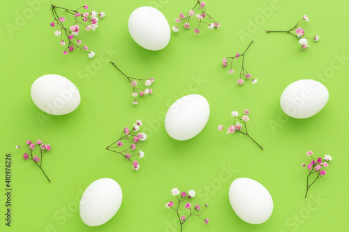 White Easter Eggs on green background with pink gypsophila , Fun Easter flat lay.