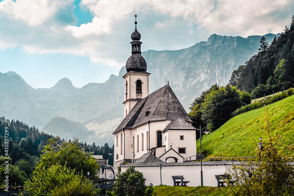 Amazing alpine landscape in the Bavarian Alps with the church of St. Sebastian in the national park Berchtesgaden. The church is standing in a valley surrounded by forested hills and rough mountains.