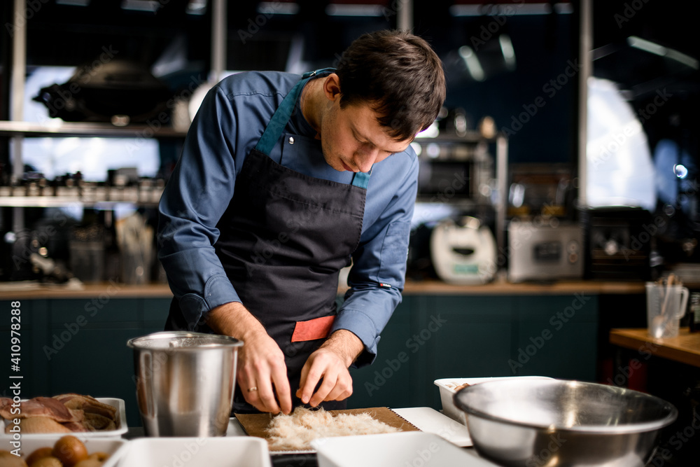 view of male chef who lays ingredients for dish on cutting board at restaurant kitchen view of male chef who lays ingredients for dish on cutting board at restaurant kitchen