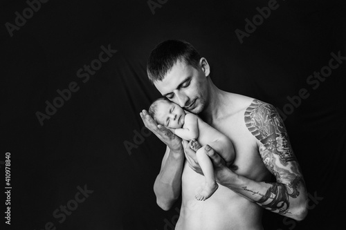 4. Father with tattoo on his arm is holding his newborn baby girl on a black and white background