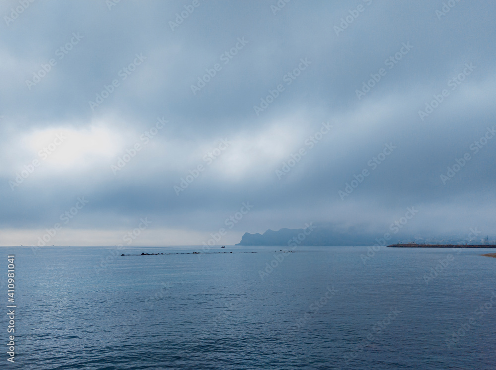 Landscape of the Mediterranean Sea from the coast of Altea in Valencia (Spain). In a calm sea you can see a small fishing boat under a cloudy sky through which the sun's rays filter