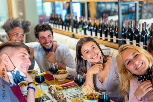 group of millennials friends having dinner in a restaurant, reopening of food service after lockdown, extended family and diversity people drinking wine and making selfie, focus on brunette woman