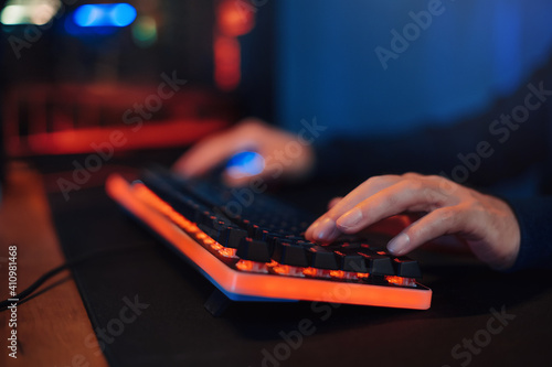 Close up of gamer's hands on keyboard, pushing buttons, playing video games online. Hacker uses keyboard, shakes buttons with fingers to crack password. Internet security, cyber attack. Neon color