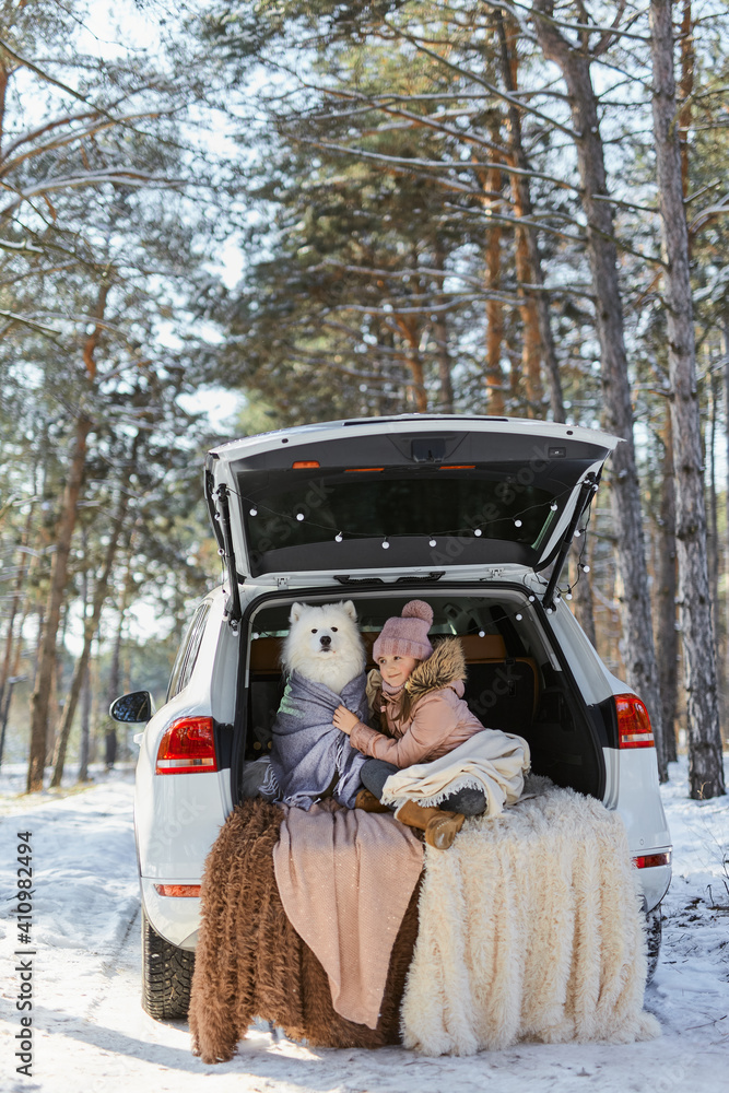 Child girl sitting in the trunk of car with her pet