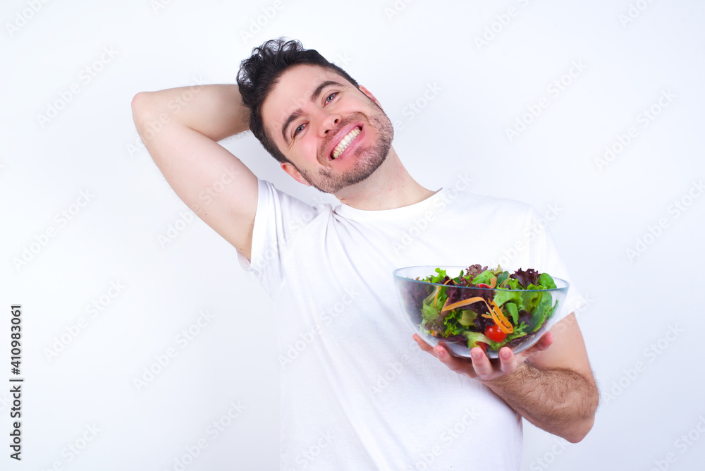 Young handsome Caucasian man holding a salad bowl against white background stretching arms, relaxed position. Young handsome Caucasian man holding a salad bowl against white background stretching arms, relaxed position.