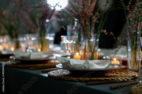 Table decorated with genista flowers and bergrass. Serving with wicker coasters for plates  napkins  burning candles and glasses. Decorations and table for wedding and dinner parties.