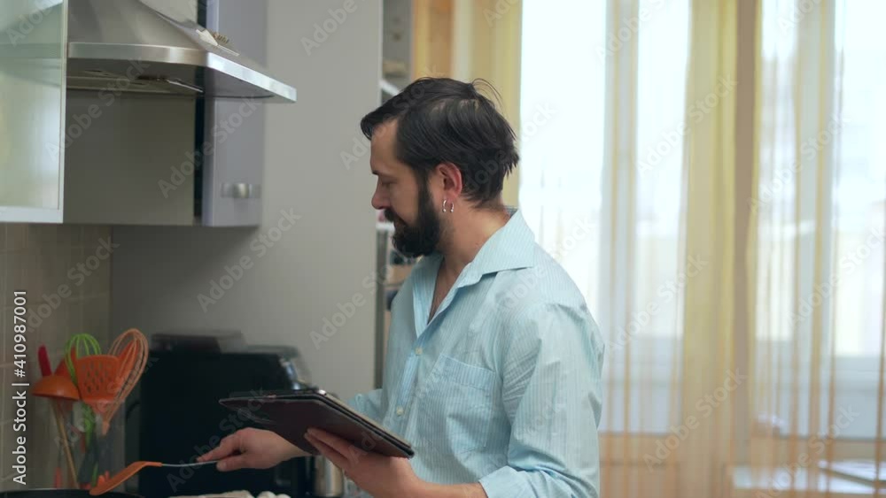 Man in kitchen cooking dish and using digital tablet Man in kitchen cooking dish and using digital tablet