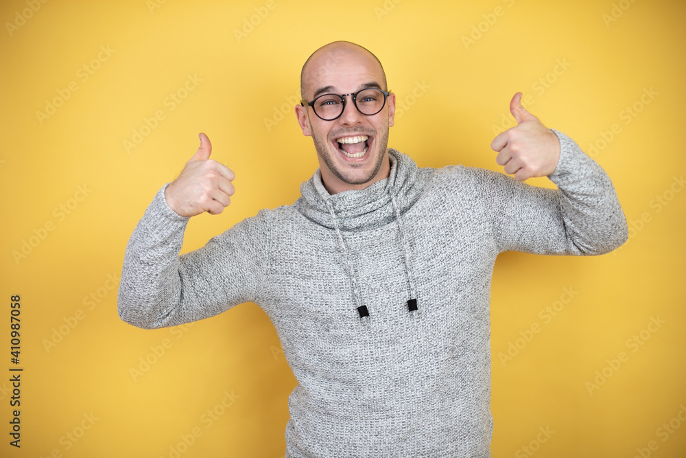 Naklejka premium Young bald man wearing glasses over yellow background smiling and doing the ok signal with his thumbs