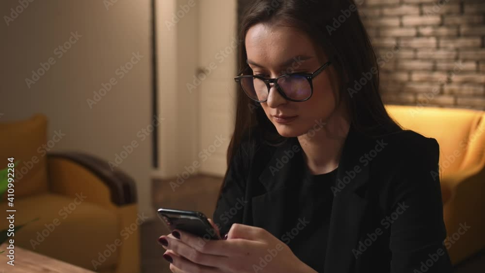 Attractive young woman in glasses using phone for online shopping in social media, technology mobile message communication at home or office. Slow motion
