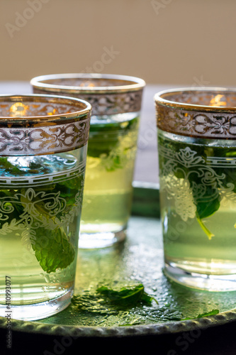 Close-up of three glasses with arabic tea and mint on green plate, on rustic wooden table, in vertical, with copy space
