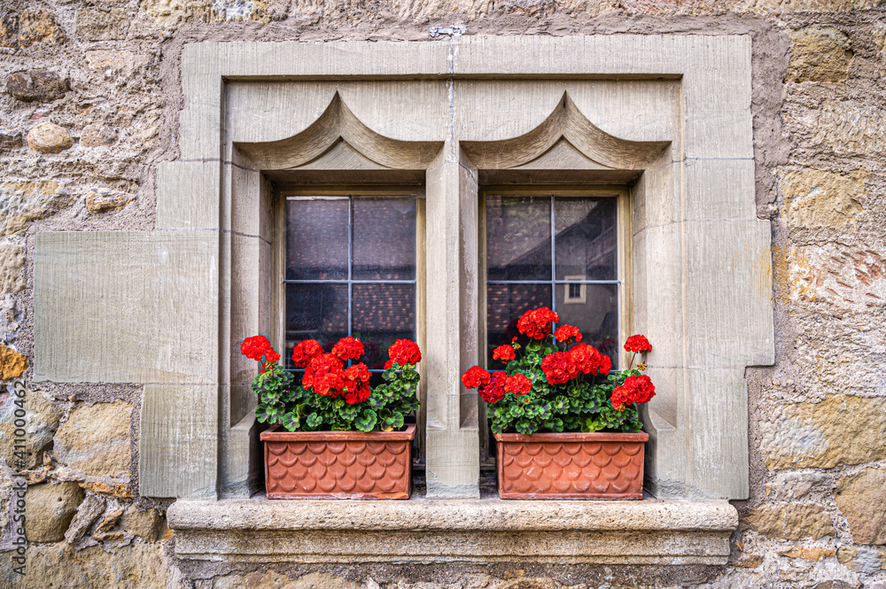 Old window in a medieval house wall with red geranium on the windowsill