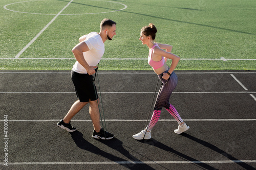 Young fitness couple trains at the stadium in the summer with an elastic expander