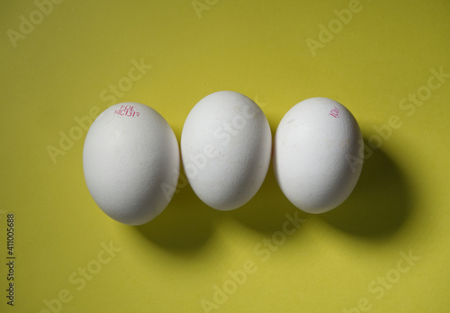 Three white bio eggs on yellow background, topview