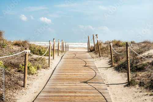 Camino de aceso de madera a la playa rodeado de dunas en la costa del mar mediterraneo en una playa  de Canet de Berenguer en Valencia, España. 