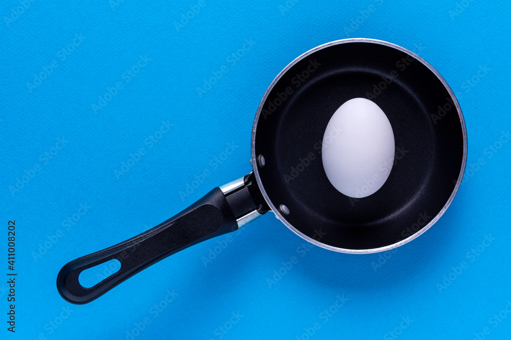 A small frying pan with a white egg on a blue background A small frying pan with a white egg on a blue background