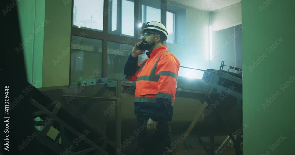 Factory worker speaking on smartphone near conveyor belt Factory worker speaking on smartphone near conveyor belt