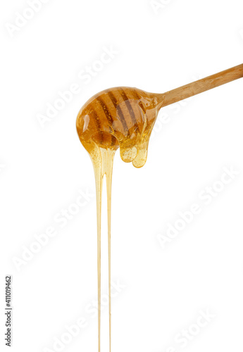 Close up honey flowing from wooden dipper on white