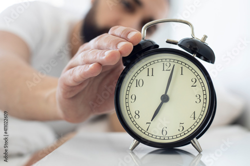 Man lying in bed, turning off the alarm clock at 7 in the morning.