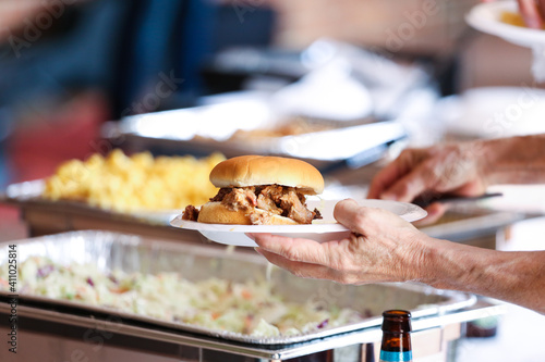 A person dishing up a pork sandwich at catering on a white plate. 