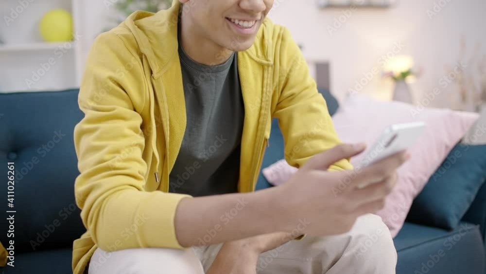 Cheerful mixed-race teen male smiling, using online app on smartphone at home Cheerful mixed-race teen male smiling, using online app on smartphone at home