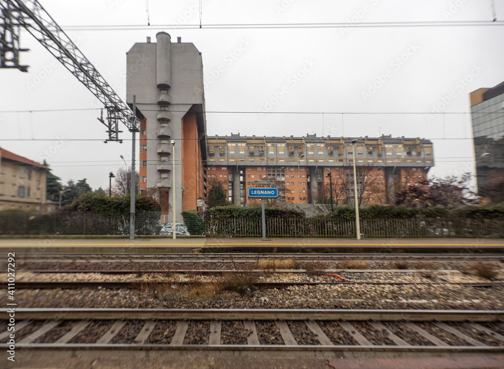 Railway tracks with popular buildings in the background of an old station in the run-down outskirts of an Italian town.