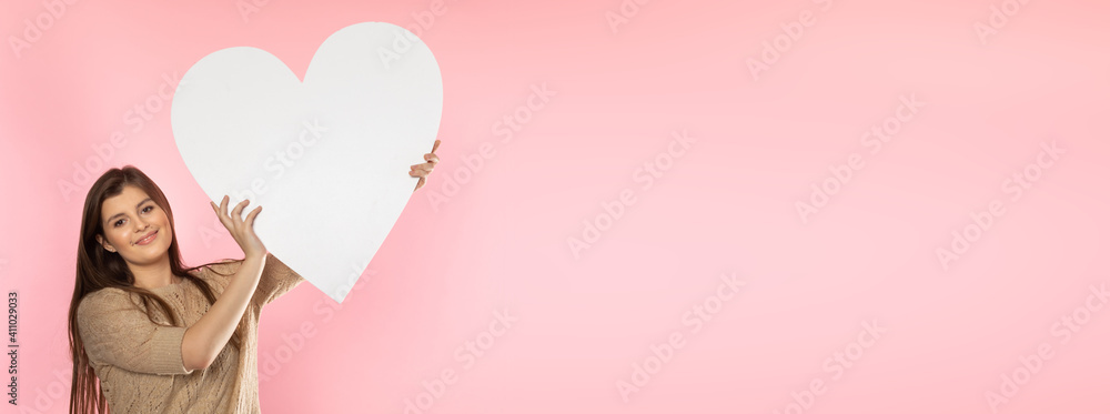 Girl with a large white heart shape in the hands. A student in love stands and holds a large heart shape in her hands. Valentine's Day and love. Panoramic frame. Girl with a large white heart shape in the hands. A student in love stands and holds a large heart shape in her hands. Valentine's Day and love. Panoramic frame.