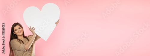 Girl with a large white heart shape in the hands. A student in love stands and holds a large heart shape in her hands. Valentine's Day and love. Panoramic frame.