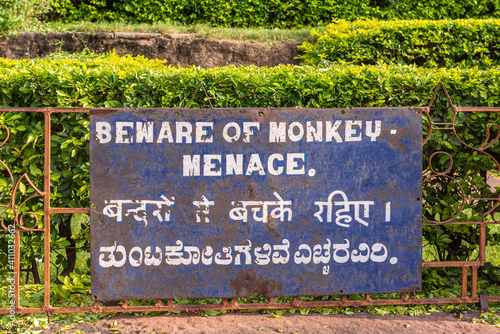 Badami, Karnataka, India - November 7, 2013: Cave temples above Agasthya Lake. White on blue large warning sign: Beware of Monkey Menace, in 3 languages including Hindi and Kannada. photo