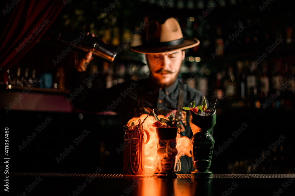 fancy glass with cocktail stands on bar and bartender setting it on fire at background