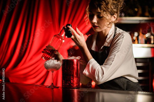 young beautiful female bartender pours drink from jigger into large cup. photo