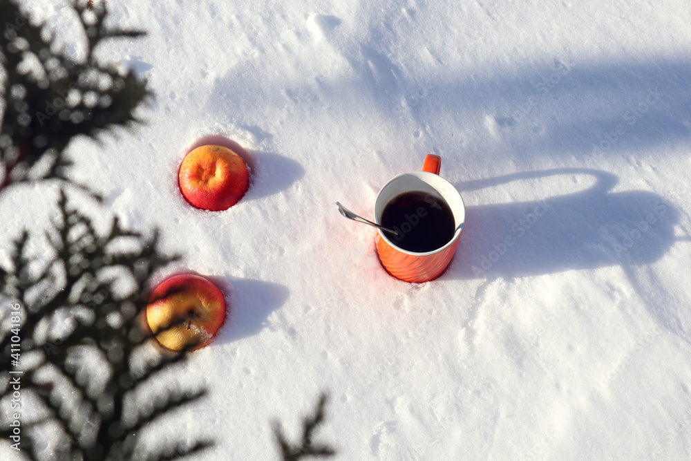Orange cup with two red apples on the snow, top view, bokeh-the concept of a pleasant holiday on a winter day Orange cup with two red apples on the snow, top view, bokeh-the concept of a pleasant holiday on a winter day