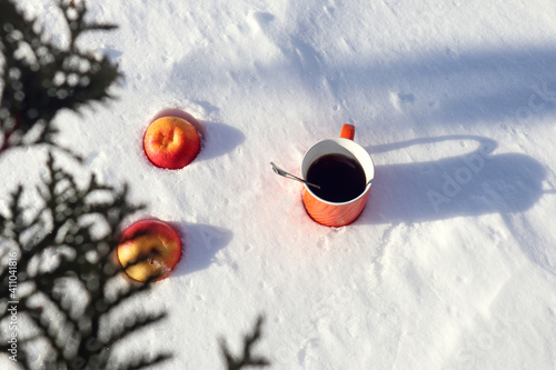 Orange cup with two red apples on the snow, top view, bokeh-the concept of a pleasant holiday on a winter day