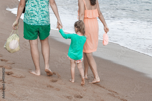 A family walks along the beach barefoot. Mom and dad hold their daughter's hand. The concept of relations.