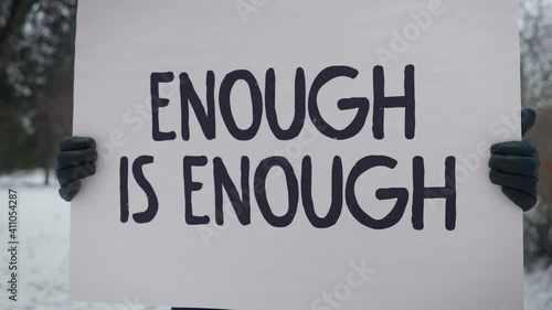 A person wearing gloves is holding a banner Enough is enough. He is protesting about the unlawful behaviour of the current government and the police brutality. Single picket. photo