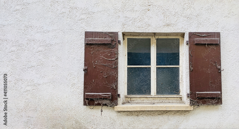 Alte Hauswand mit Quadratischem Sprossenfenster, rechts und links braune alte Holzläden und Fenstersims