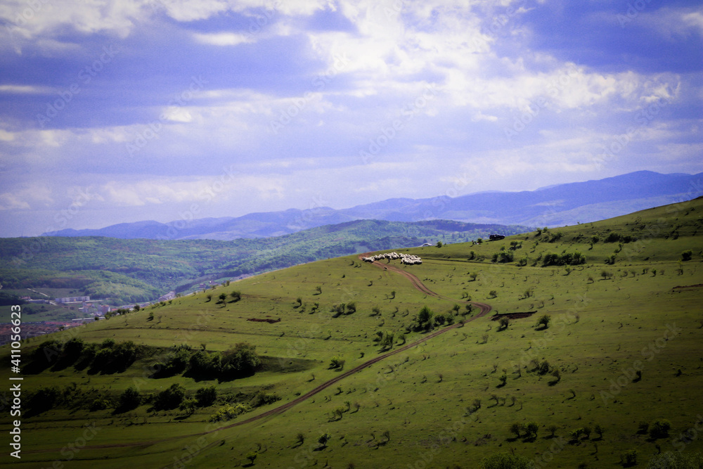 Beautiful landscape of a hill and scenery of the hill and mountains behind and om top of the hill are sheep Beautiful landscape of a hill and scenery of the hill and mountains behind and om top of the hill are sheep